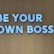 Large white letters spelling 'BE YOUR OWN BOSS' are mounted on a wooden wall, conveying empowerment and independence.